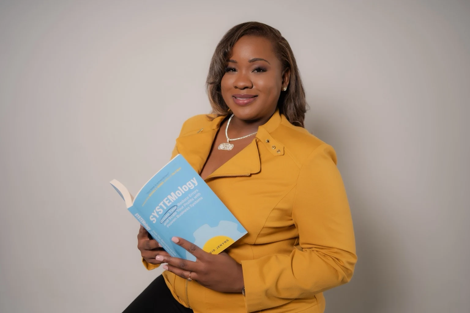 Nichellee Marsh in a mustard jacket holding the SYSTEMology book